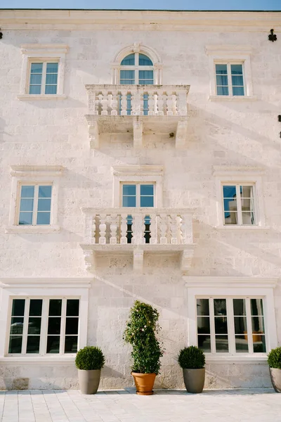 Fachada de construção de pedra branca com varandas e vasos de flores em um piso de azulejos — Fotografia de Stock