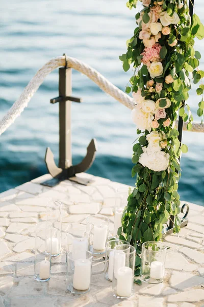 Rack of a wedding arch on a cobbled pier by the sea, surrounded by candles in glasses — Stock Photo, Image