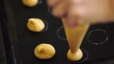 Pasta şefi choux au craquelin 'i bir hamur torbasından silikon bir paspasın üzerindeki kupalara sıkıştırıyor.