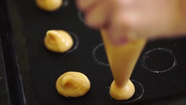 Pastelero exprime choux au craquelin de una bolsa de pastelería en tazas en una estera de silicona — Vídeo de stock