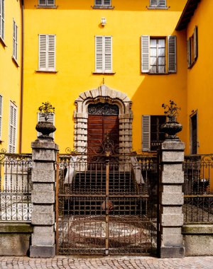 Sarı panjurlu bir evin önünde çit dövülmüş.