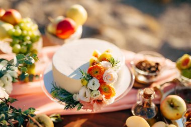 Çiçeklerle süslenmiş düğün pastası masanın üzerinde duruyor. 