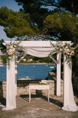 Kayıt masası deniz kenarında çiçeklerle süslenmiş bir düğün tentesinin altında duruyor.