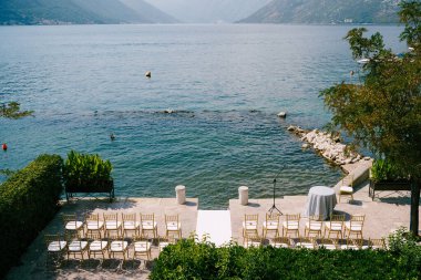 Beyaz sandalyeler rıhtımda, kayıt masasının yanında suyun yanında duruyor.