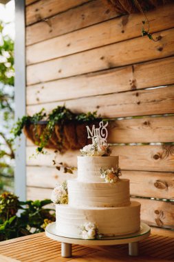 Tahta bir masanın üzerinde çiçeklerle süslenmiş üç katlı düğün pastası.