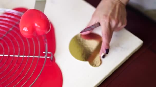 Chef gebruikt een spatel en een mes om een hartvormige taart op een gouden ondergrond te leggen. — Stockvideo