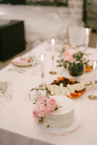 Λευκή γαμήλια τούρτα στέκεται σε ένα πιάτο στο τραπέζι δίπλα σε αναμμένα κεριά — Φωτογραφία Αρχείου