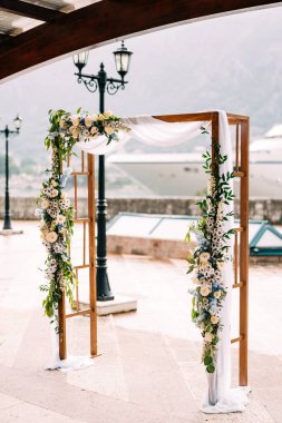 Çiçek ve kumaşla süslenmiş dikdörtgen ahşap kemer setin üzerinde bir fenerin yanında duruyor.