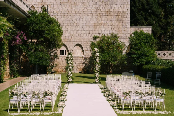 Alfombra blanca corre entre filas de sillas decoradas con flores al medio arco de la boda — Foto de Stock