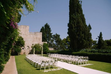 Yeşil bahçedeki çiçeklerle süslenmiş sandalyeler arasında beyaz halı.
