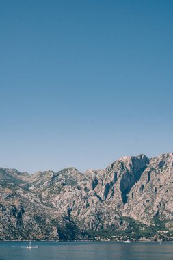 Mavi gökyüzünün arka planına karşı Kotor Körfezi kıyısında büyük bir sıradağ.