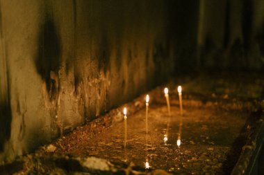 Candles are burning on a stand in front of a wall in a church clipart