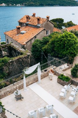 Beyaz sandalyeler bir düğün kemerinin önünde durur. Çiçek ve kumaşla süslenmiştir.