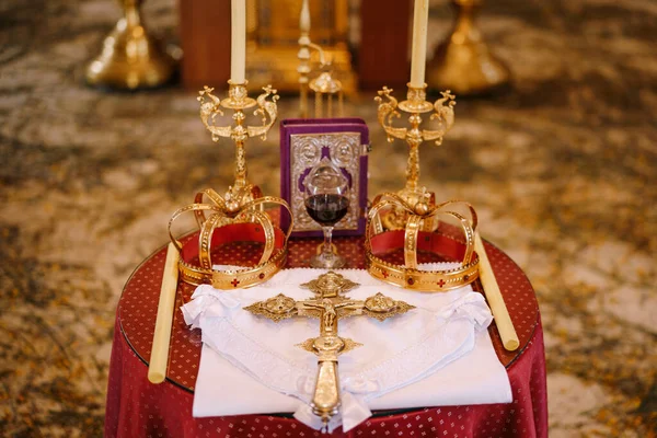 Kříž, zlaté koruny a svícny stojí na stole v kostele — Stock fotografie