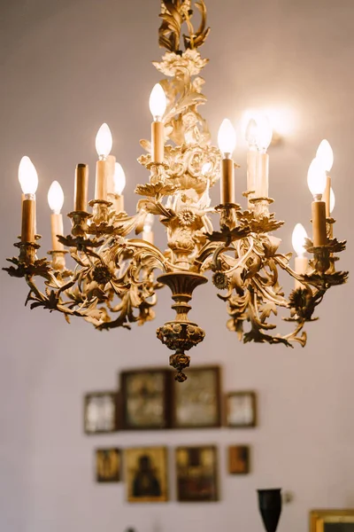 Золотая люстра с лампочками, висящими в церкви на фоне стены с иконами — стоковое фото