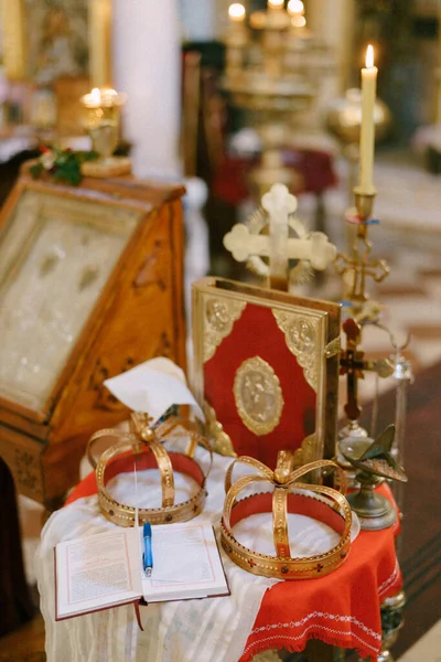 Korset, guldkronor, en bibel och ljusstakar finns på bordet i kyrkan — Stockfoto