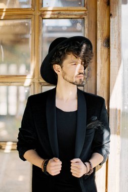 Ahşap bir pencerenin arkasında siyah şapkalı genç adam.