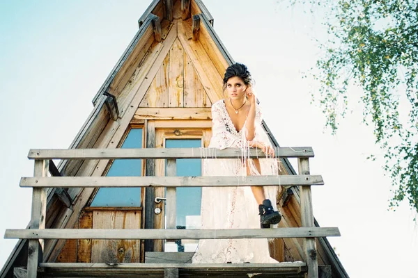 花嫁は木製の手すりにもたれて三角形の家のバルコニーに立つ — ストック写真