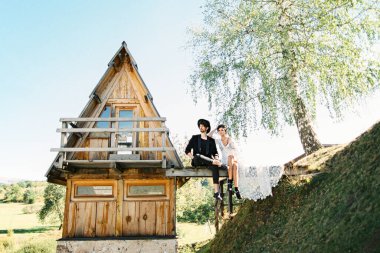 Gelin ve damat, üçgen bir evin yakınındaki tahta köprüde otururlar.