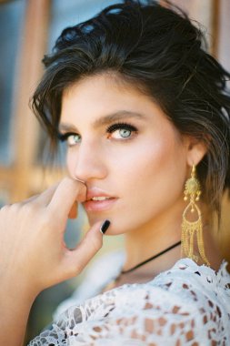 Beyaz hasır elbiseli genç kız parmaklarıyla çenesine dokunuyor. Portre