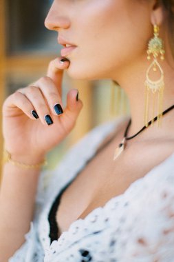 Beyaz elbiseli kadın parmaklarıyla çenesine dokunuyor. Yakın plan.