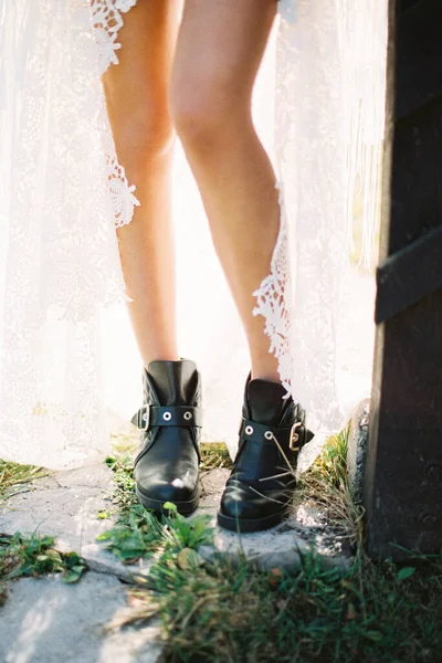 Les jambes de mariée en bottes noires jaillissent de la fente d'une robe en osier blanc. Gros plan — Photo