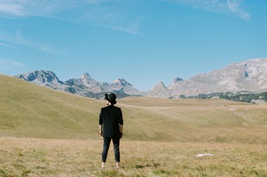 Siyah şapkalı bir adam vadide duruyor ve dağlara bakıyor. Arka plan