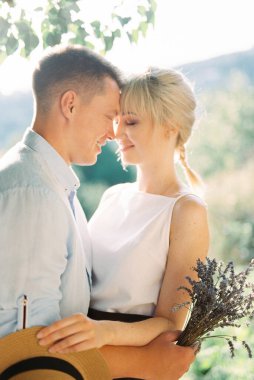 Lavanta buketli gülümseyen adam hasır şapkalı kadını kucaklıyor.