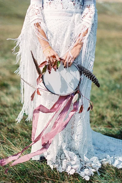 Ταμπουρίνη με κορδέλες και φτερά στα χέρια μιας γυναίκας με λευκό φόρεμα — Φωτογραφία Αρχείου