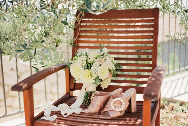 Ramo de boda está en un sillón de madera junto a las sandalias de la novia —  Fotos de Stock