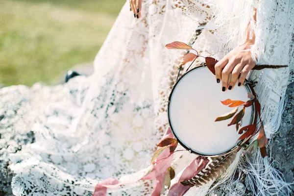 Pandeireta decorada com penas e fitas na mão de uma mulher em um vestido — Fotografia de Stock