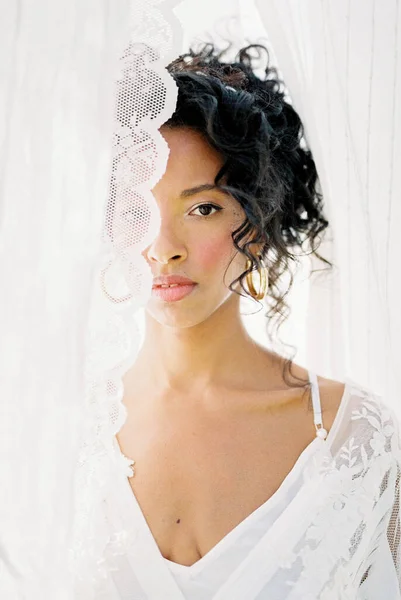 Retrato de uma mulher em um vestido branco espreitando por trás de uma cortina Fotos De Bancos De Imagens