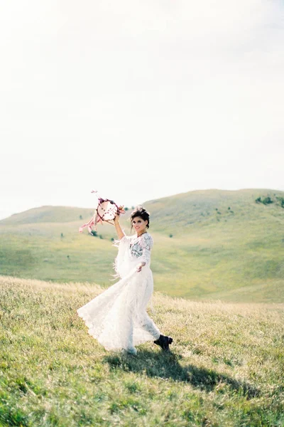 Menina em um vestido branco caminha através de um vale verde, levantando um tamboril acima de sua cabeça — Fotografia de Stock