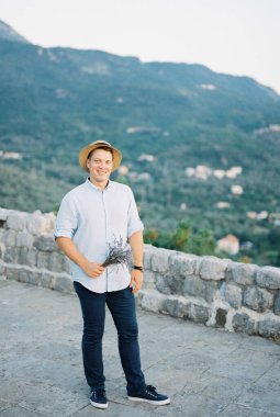 Hasır şapkalı adam dağlara bakan gözlem güvertesinde duruyor.