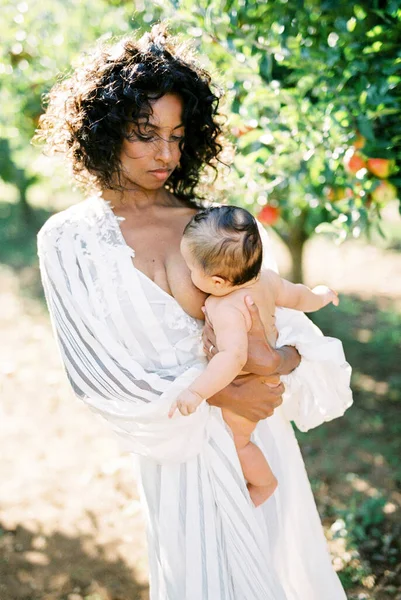 Bir kadın bahçede bebeğini emziriyor.