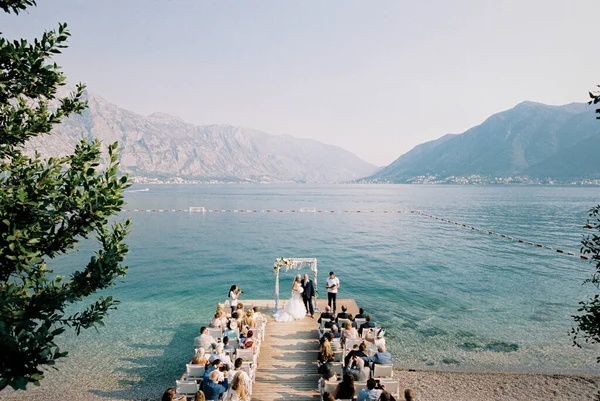 Kotor, Montenegro 23.06.21: Brilho e noiva ficam perto do arco de casamento na frente dos convidados na praia — Fotografia de Stock
