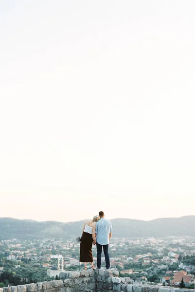 Woman put her head on the man shoulder on a stone wall overlooking the mountains. Back view — Stock Photo, Image