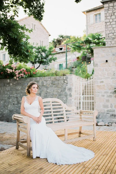 Menyasszony egy fehér sellő ruha ül egy fa padon az udvaron a villa — Stock Fotó