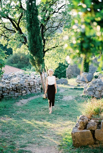 Γυναίκα με ένα μπουκέτο λεβάντας στο χέρι της περπατά σε ένα πράσινο πάρκο ανάμεσα στις πέτρες — Φωτογραφία Αρχείου