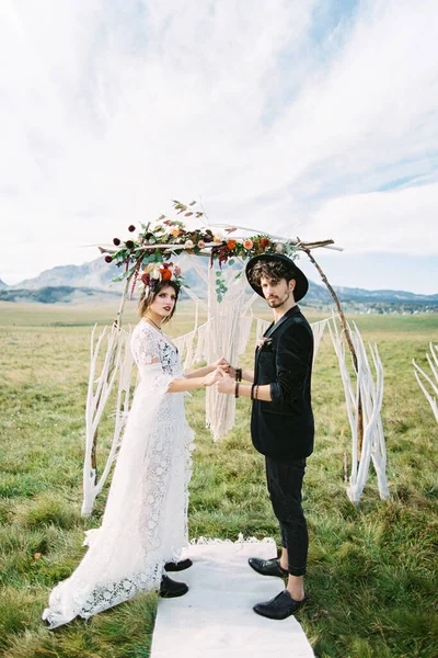 Noiva e noivo de pé de mãos dadas perto do arco de casamento — Fotografia de Stock