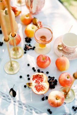 Nar ve elmalar, mumların yanındaki masada beyaz bir masa örtüsünün üzerinde yatar.