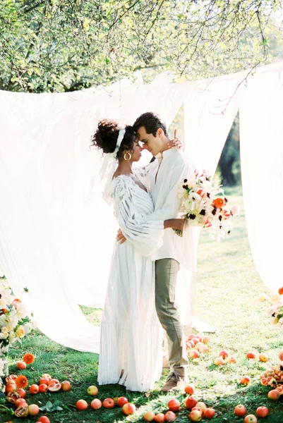 Homem abraçando mulher com buquê no jardim perto de cortinas brancas — Fotografia de Stock