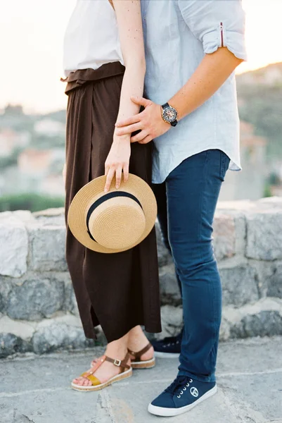 El hombre abraza a la mujer por detrás mientras está de pie junto a una valla de piedra contra un fondo de montañas —  Fotos de Stock