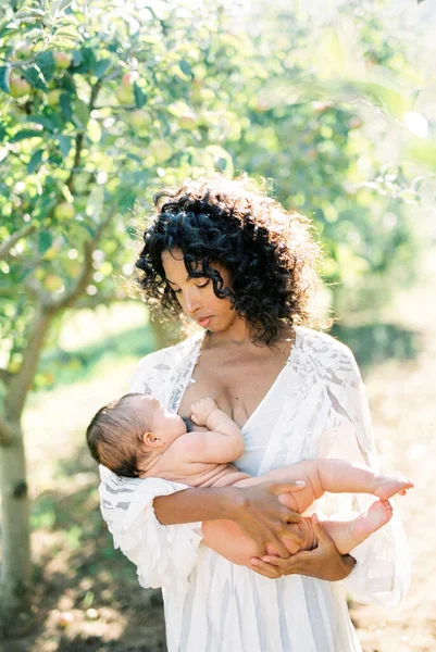 Beyaz elbiseli bir anne onu kollarında tutan bir bebeği emziriyor. — Stok fotoğraf