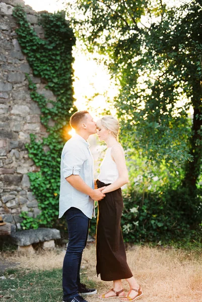 Homme embrasse femme sur le front tout en se tenant près d'un mur de pierre entrelacé avec lierre — Photo