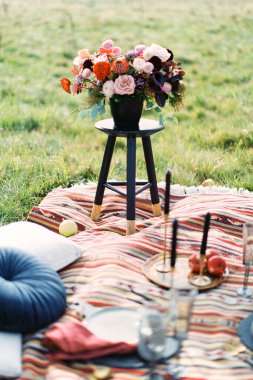 Vazodaki düğün buketi renkli bir yatak örtüsünün üzerindeki taburede duruyor.