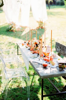 Bahçede mumlar, meyveler ve fincanlarla kaplı beyaz bir masa örtüsü.