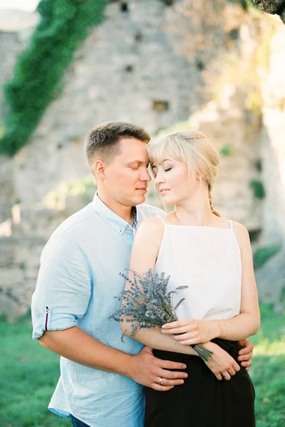 Mann umarmt Frau mit Lavendelstrauß nahe einer Steinmauer — Stockfoto
