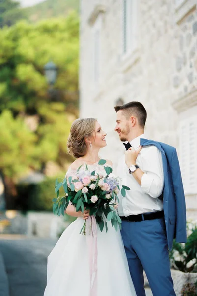 Vőlegény és menyasszony egy csokor virággal állnak a kőépület mellett. — Stock Fotó