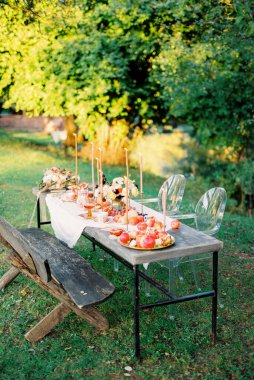 Yeşil bir bahçede içinde mumlar ve ikramlar olan bir masa.